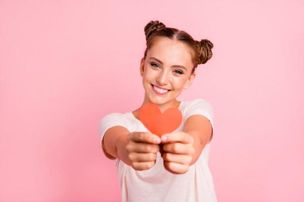 O femeie zâmbeşte şi ţine în mâini o inimă din carton roşu
