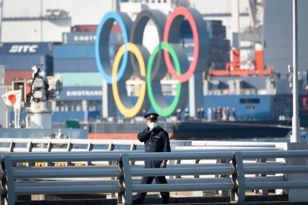 Un ofițer de poliție patrulează lângă simbolul olimpic transportat pe o barjă în secțiunea Odaiba, la Tokyo