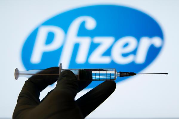 Seringă medicală în față și logo-ul companiei Pfizer estompat în fundal