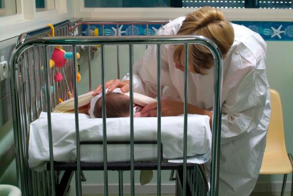 O femeie stă lângă patul unui nou-născut
