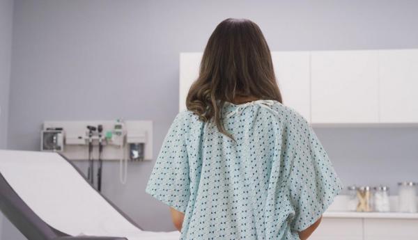 Femeie stând cu spatele pe un pat de spital