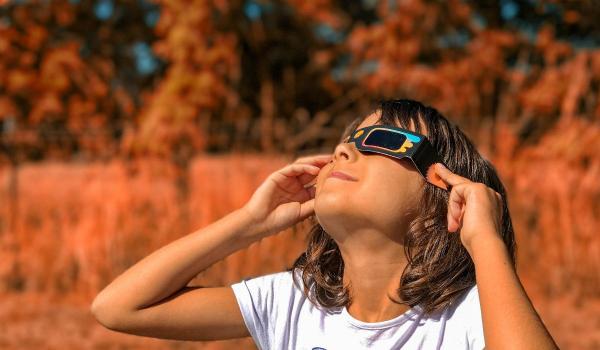 O fetiţă urmăreşte eclipsa de soare prin ochelarii cu lentile speciale.