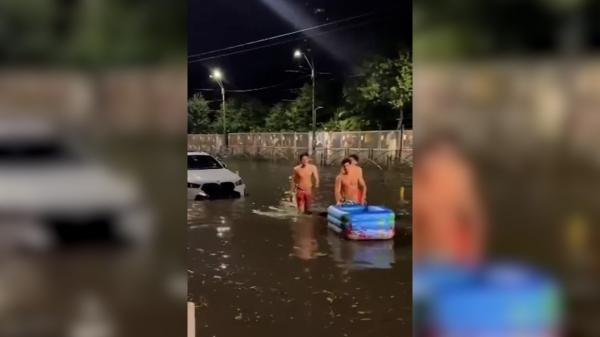 Momentul în care trei tineri traversează apa până la genunchi, în București, cu o saltea