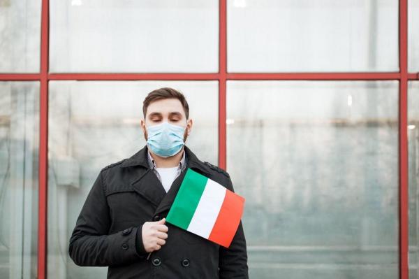 Un tânăr cu mască ţine în mână steagul italian