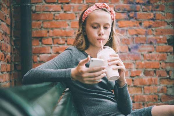 O tânără îşi foloseşte telefonul mobil în timp ce bea cu paiul dintr-o băutură răcoritoare