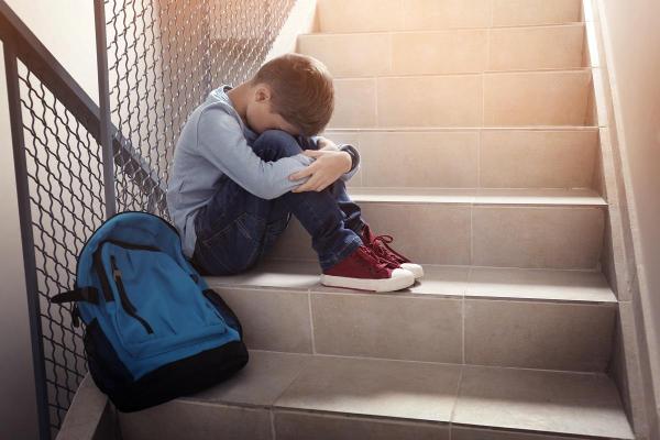 Şcolar aşezat pe scări, cu ghiozdanul lângă el