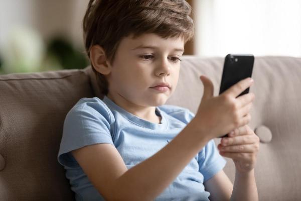 În Imagine: Un băiat se joacă pe telefonul mobil