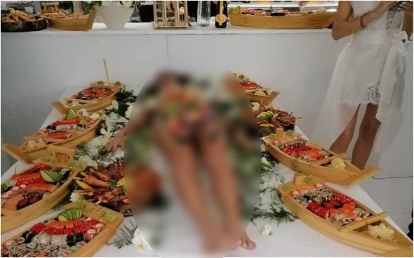 O tânără în costum de baie a fost așezată pe masă ca suport pentru platourile de sushi