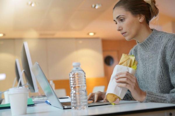 O femeie mănâncă în fața unui laptop