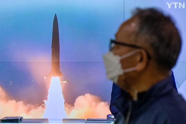 Un bărbat stă lângă un ecran TV care arată o emisiune de știri cu filmări ale unui test de rachetă nord-coreean