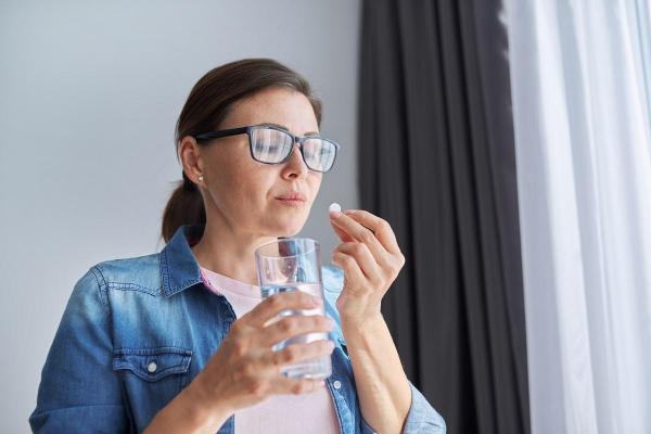 Femeie cu un pahar de apa în mână şi cu o pastilă