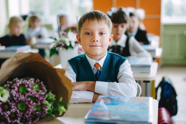 Elev în prima zi de şcoală, cu un buchet de flori pe bancă