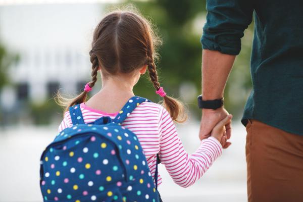 O fetiţă este dusă de mână de tatăl ei la şcoală, în clasa pregătitoare
