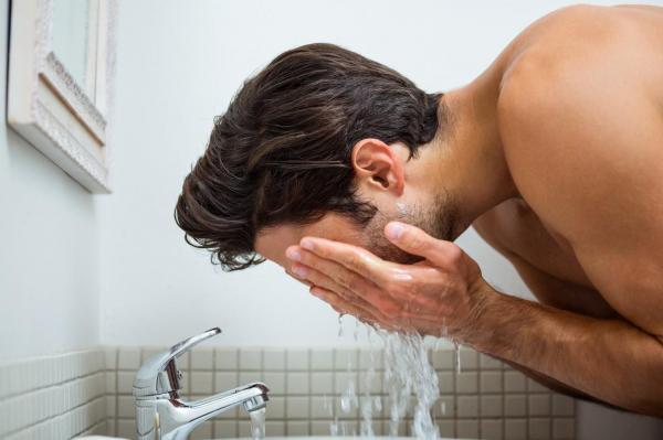 bărbat la bustul gol care se spală pe faţă cu apă de la chiuvetă