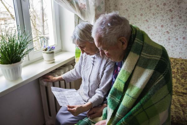 Persoane în vârstă lângă un calorifier citind o factură, imagine cu scop ilustrativ